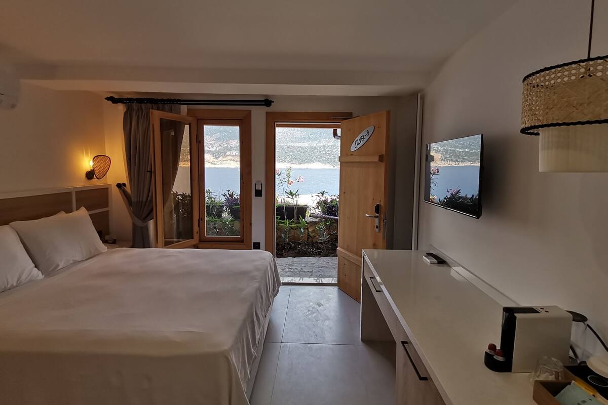 A hotel room with a bed, a desk, a TV, and a view of the sea.
