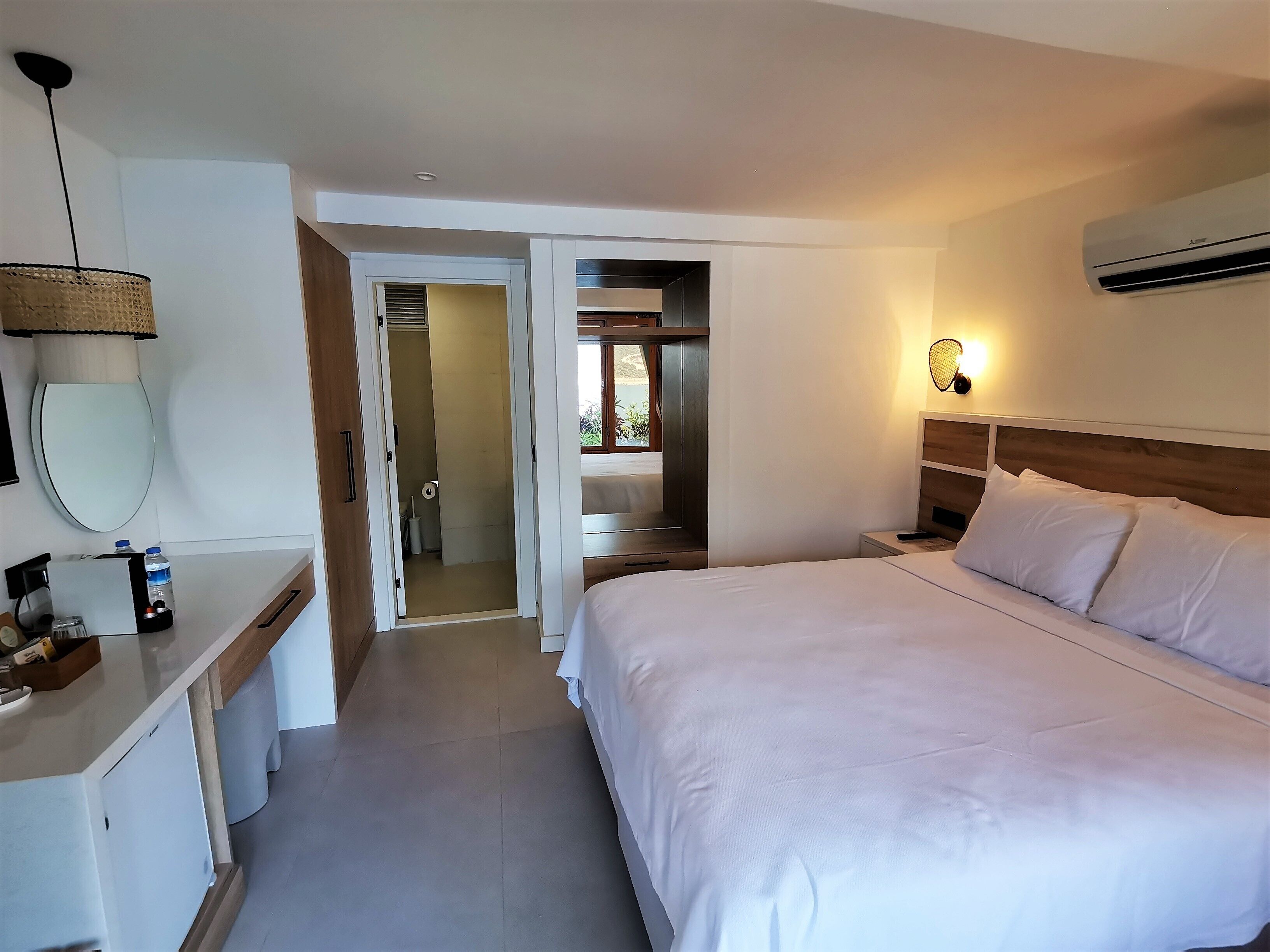 Ein Hotelzimmer mit einem großen Bett, einem Nachttisch mit Lampe, einem Spiegel und einer Klimaanlage.