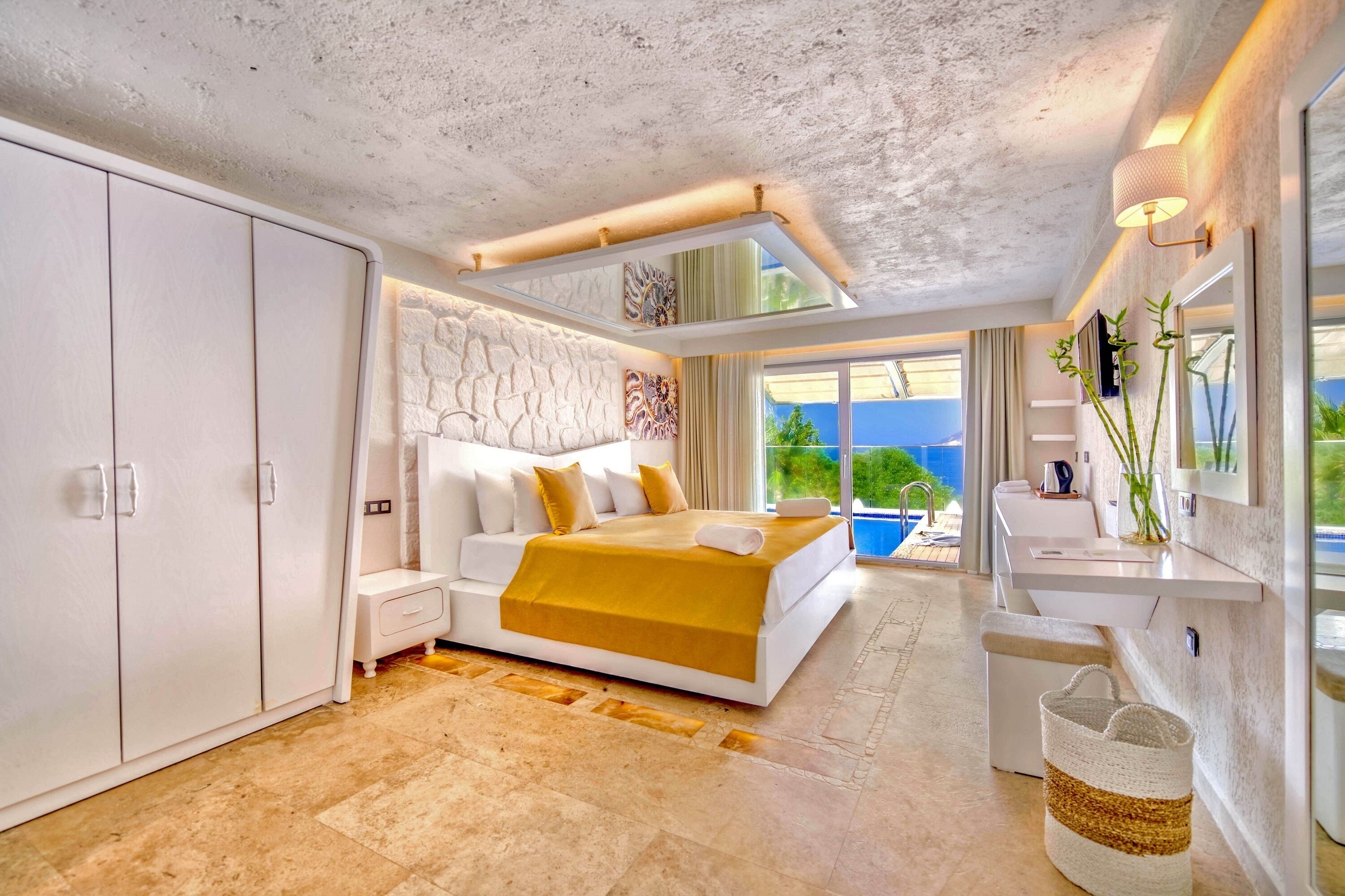A modern bedroom with a large bed, a wardrobe, a bathroom with a sink and mirror, and a view of the outdoors.