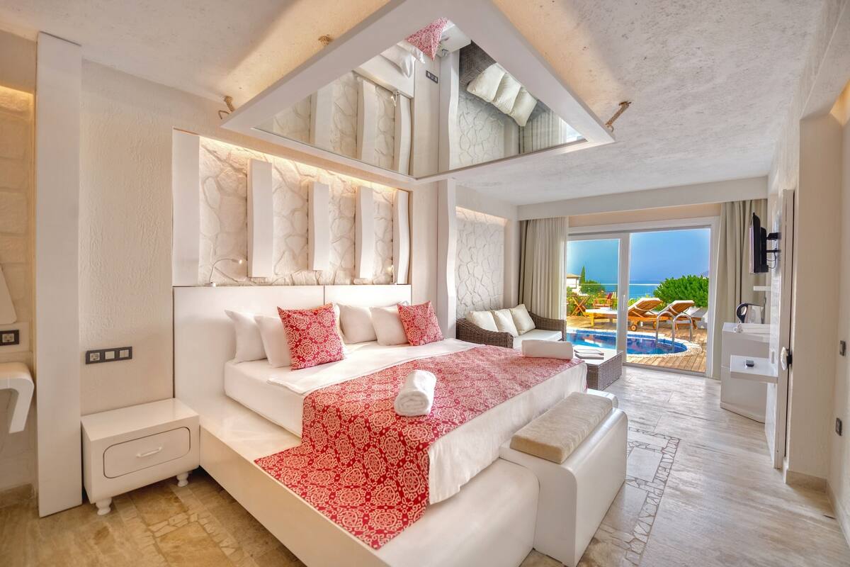A modern hotel room with a large bed, a small sofa, a nightstand, and a view of the pool and ocean.