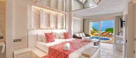 A modern hotel room with a large bed, a small sofa, a nightstand, and a view of the pool and ocean.