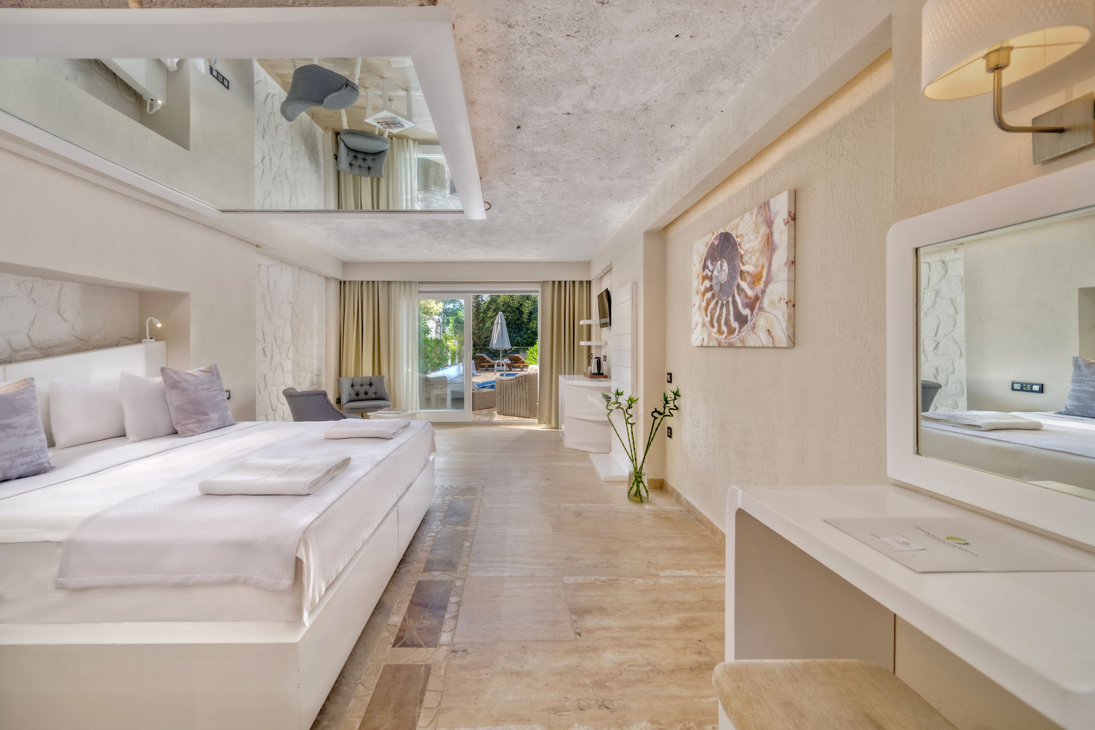 A modern hotel room with a large bed, a sitting area, a desk, and a view of the outdoors.