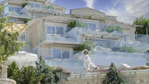 Un hotel de varios pisos con balcones, mobiliario exterior y abundante vegetación.