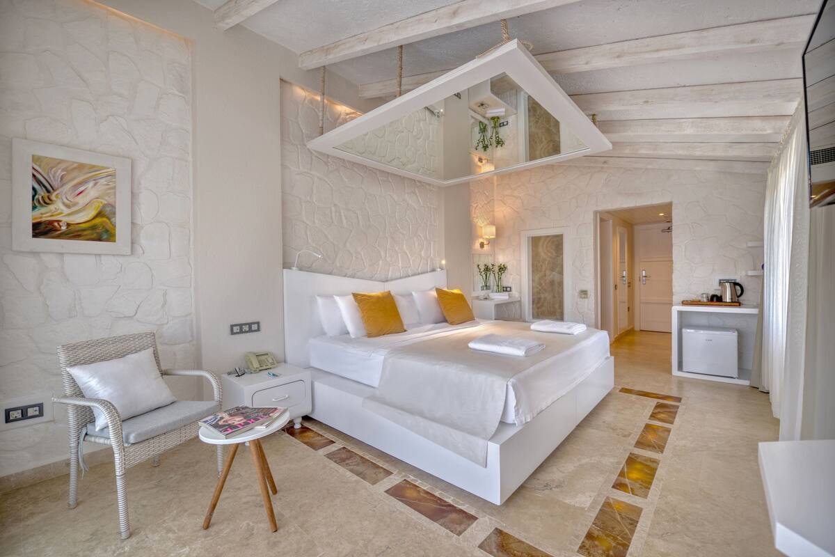 A modern bedroom with a large bed, a white chair, a bedside table, and a small desk.