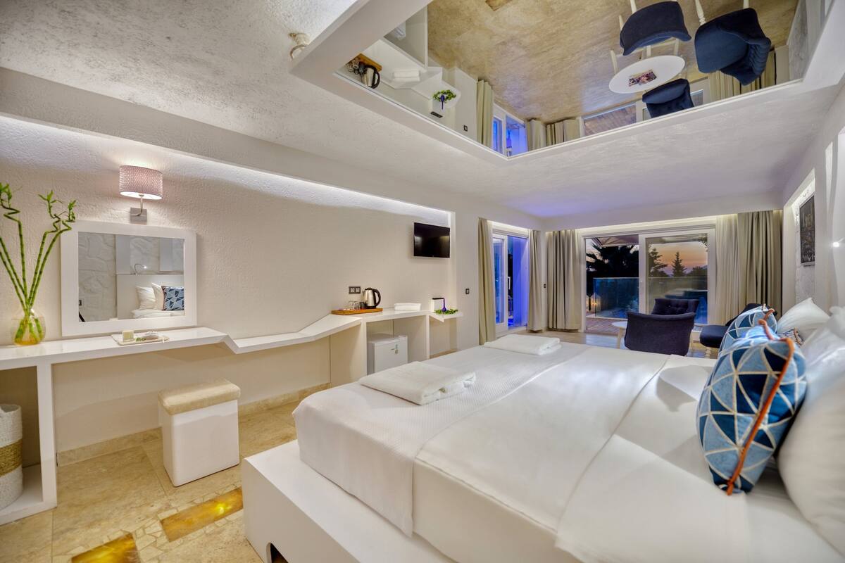 A modern hotel room with a large bed, a vanity with a mirror, and a seating area with a view of the outdoors.