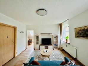 Una sala de estar con un sofá, una mesa de centro, una televisión y una estantería.