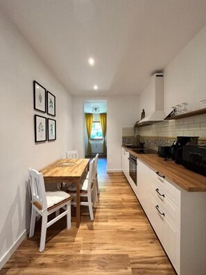 Una cocina estrecha con una mesa y sillas de madera, un armario blanco y vistas a una habitación con una cortina amarilla.