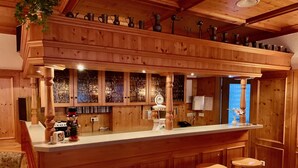 Un espace bar en bois, doté d’un comptoir, de tabourets et de différentes sortes de verres exposés sur des étagères.