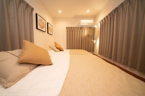 Ein Hotelzimmer mit Bett, Vorhängen, einer wandmontierten Klimaanlage und zwei gerahmten Bildern.