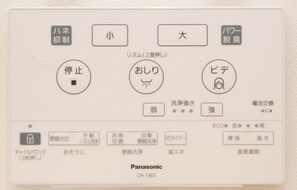 Un panneau de commande avec des étiquettes en japonais pour les réglages tels que la température de l’eau, la puissance et le mode économique.