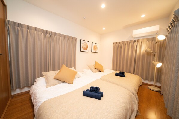 A hotel room with two beds, beige curtains, a ceiling light, and a wall-mounted air conditioner. - OneHome Shinn-Nakano (Tokyo)