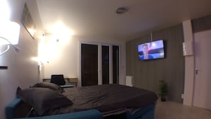 A bedroom with a bed, a desk, a chair, a TV, and a door. - Rare, Cozy "loft type" studio with terrace and garden in the heart of St Jorioz. (Saint-Jorioz)