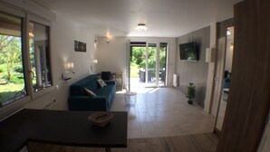 A modern living room with a sofa, a dining table, and a TV mounted on the wall. - Rare, Cozy "loft type" studio with terrace and garden in the heart of St Jorioz. (Saint-Jorioz)