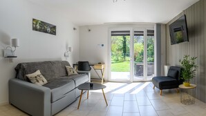 A modern living room with a grey sofa, a small round table, a black armchair, and a TV mounted on the wall. - Rare, Cozy "loft type" studio with terrace and garden in the heart of St Jorioz. (Saint-Jorioz)