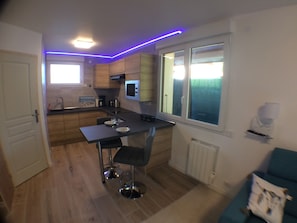 Een kleine keuken met houten kastjes, een zwart aanrecht en een raam met gordijnen.