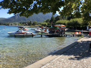 A lakeside dock with boats, a small boat house, and a paved walkway. - Rare, Cozy "loft type" studio with terrace and garden in the heart of St Jorioz. (Saint-Jorioz)