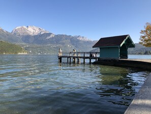 A clear lake with a wooden pier extending into the water, a small green building at the end of the pier, and mountains in the background. - Rare, Cozy "loft type" studio with terrace and garden in the heart of St Jorioz. (Saint-Jorioz)