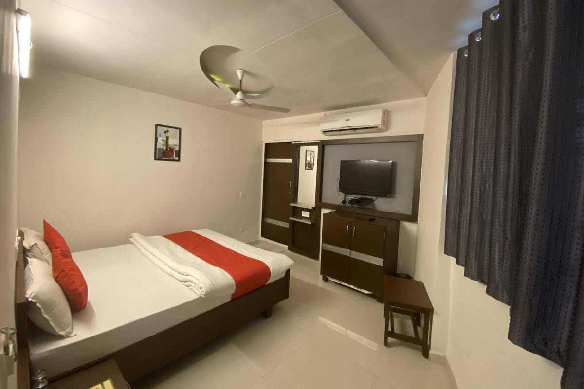 A bedroom with a bed, a TV, a wardrobe, and an air conditioning unit.