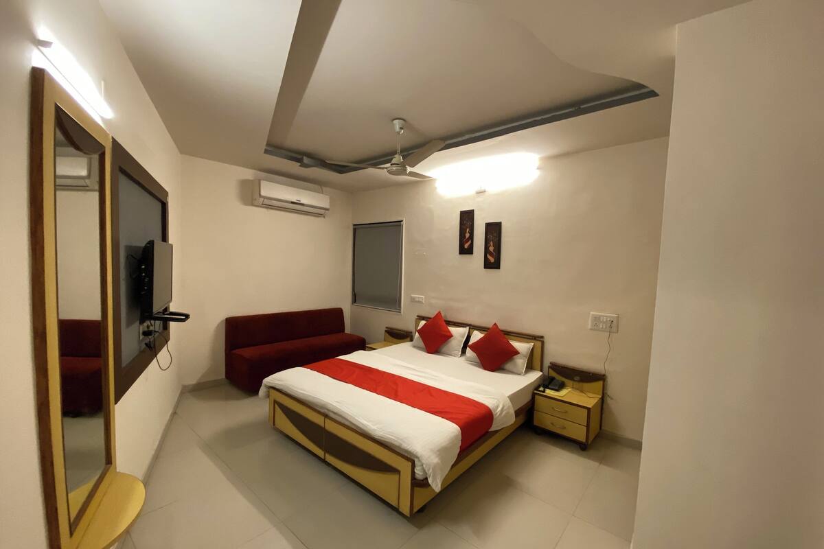 A bedroom with a bed, a red sofa, a bedside table, a nightstand, an air conditioning unit, and a ceiling fan.