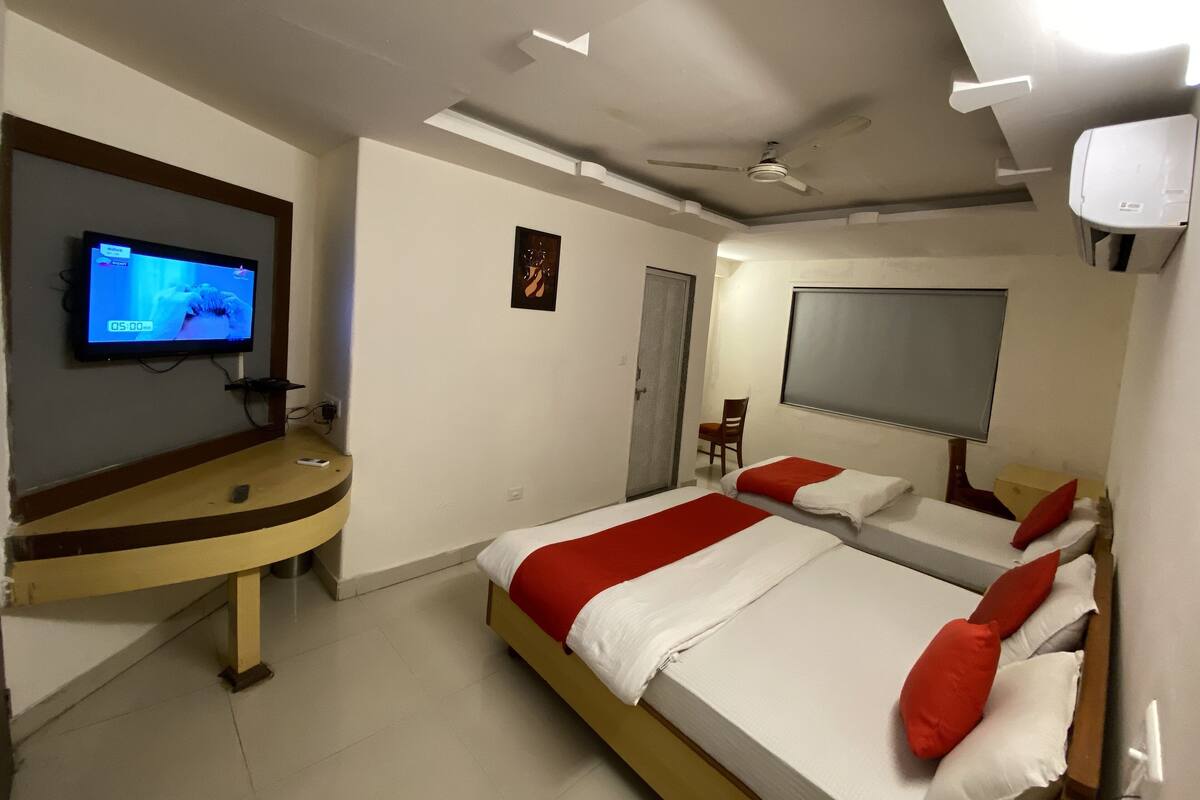 A hotel room with a TV, two beds, a desk, and a ceiling fan.