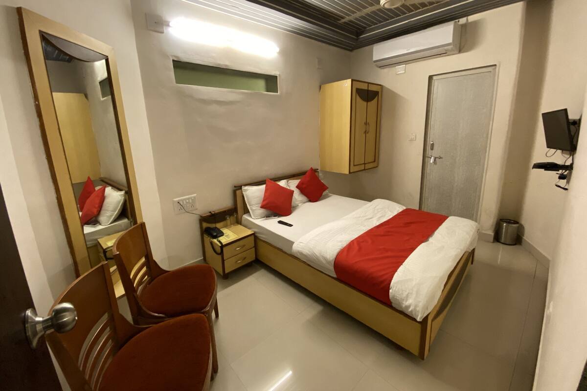 A bedroom with a bed, a wardrobe, a mirror, a desk, and a chair.