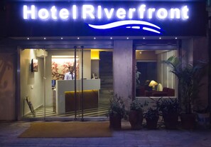 Hotel frente al río con una recepción, un recepcionista y plantas en macetas en el exterior.
