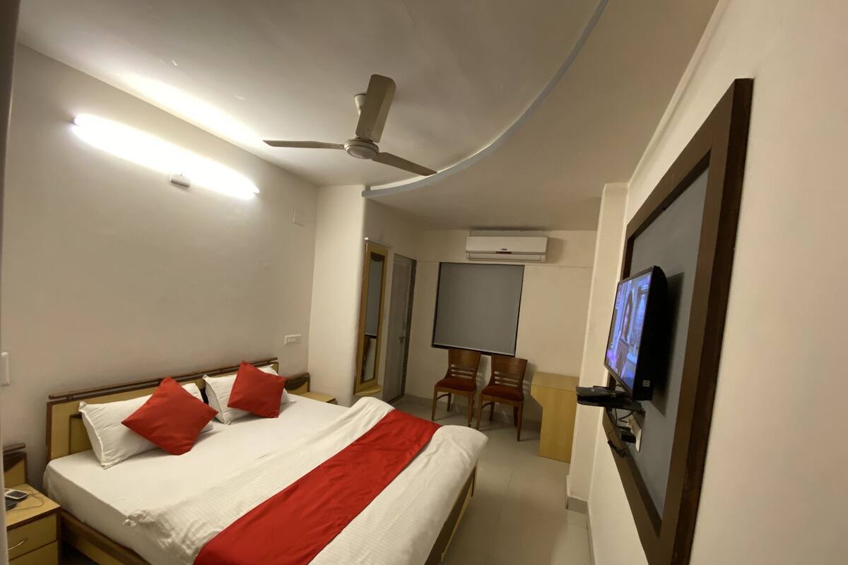 A hotel room with a bed, a TV, a ceiling fan, and an air conditioning unit.