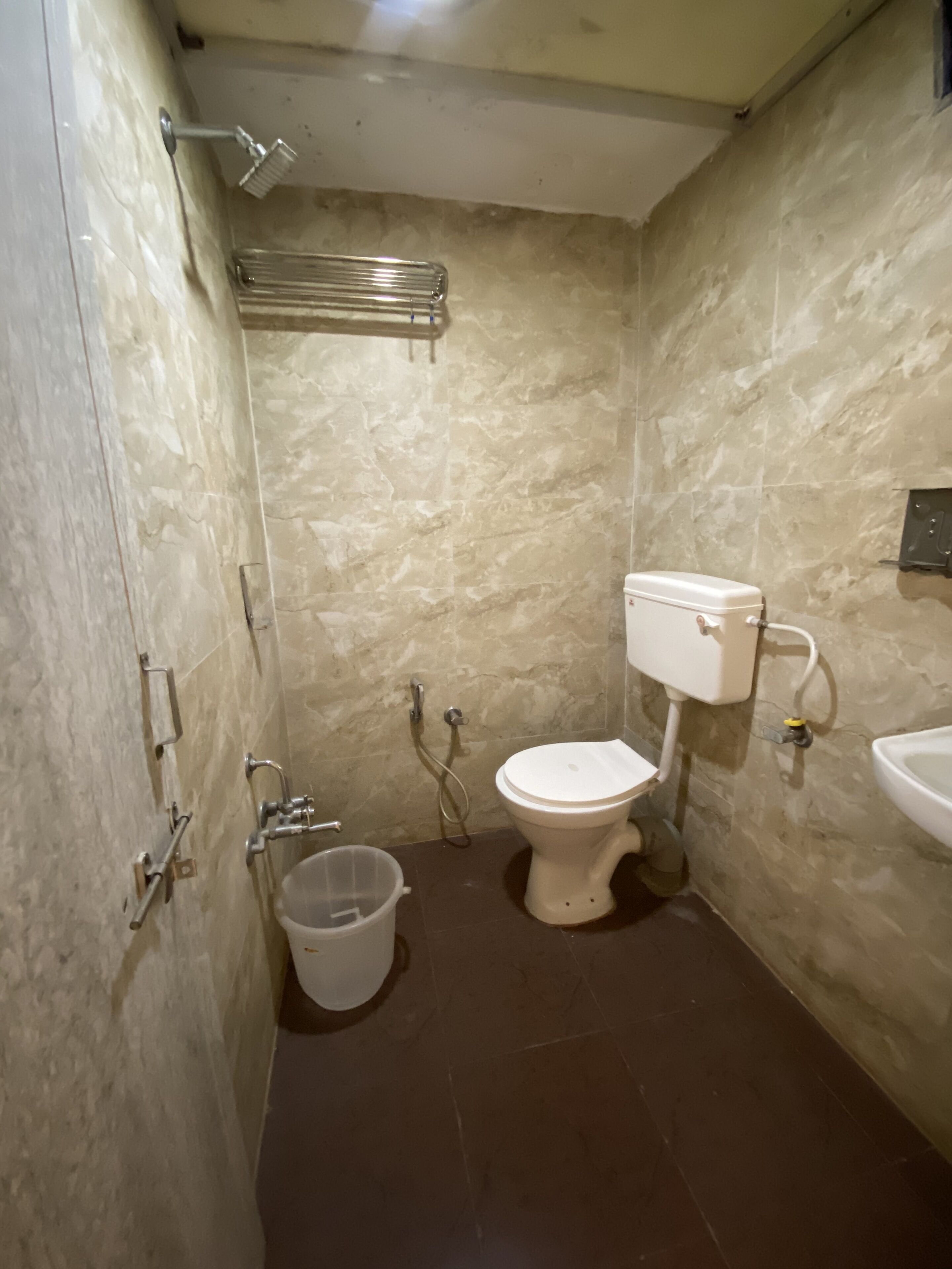 A small bathroom with a toilet, sink, shower, and a trash bin.