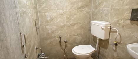 A small bathroom with a toilet, sink, shower, and a trash bin.