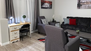 Un salon moderne avec un bureau, un canapé gris, un fauteuil noir et une petite table d’appoint agrémentée d’une plante.