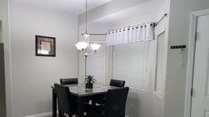 Un coin repas avec une table en marbre, des chaises noires, un lustre et une plante en pot.