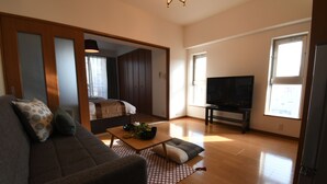 A spacious living room with a sofa, a coffee table, and a television. There is a wooden floor and a large window providing natural light. - Beau Belle Nagahori 902 (Osaka)