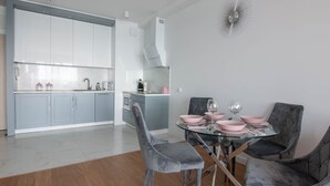 A modern kitchen with grey cabinets, a marble countertop, and a dining area with a glass table and grey upholstered chairs. - Apartament Sailor z widokiem na morze - Nadmorski Luksus (Ustronie Morskie)