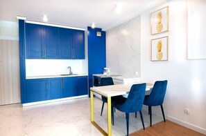 Une cuisine moderne avec des meubles bleus, un plan de travail blanc et un coin repas comprenant une table et des chaises.