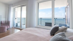 A modern bedroom with a large bed, a chair, and a view of the sea through large windows. - Apartament Sailor z widokiem na morze - Nadmorski Luksus (Ustronie Morskie)