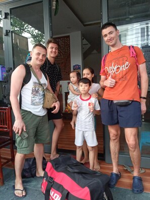 A family of five standing in a room with a glass door, a red bag on the floor, and a small table with items on it. - Lavila Hoi An Homestay (Da Nang)