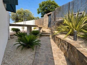 A stone pathway leading to a stone building with a wooden fence and a palm plant.