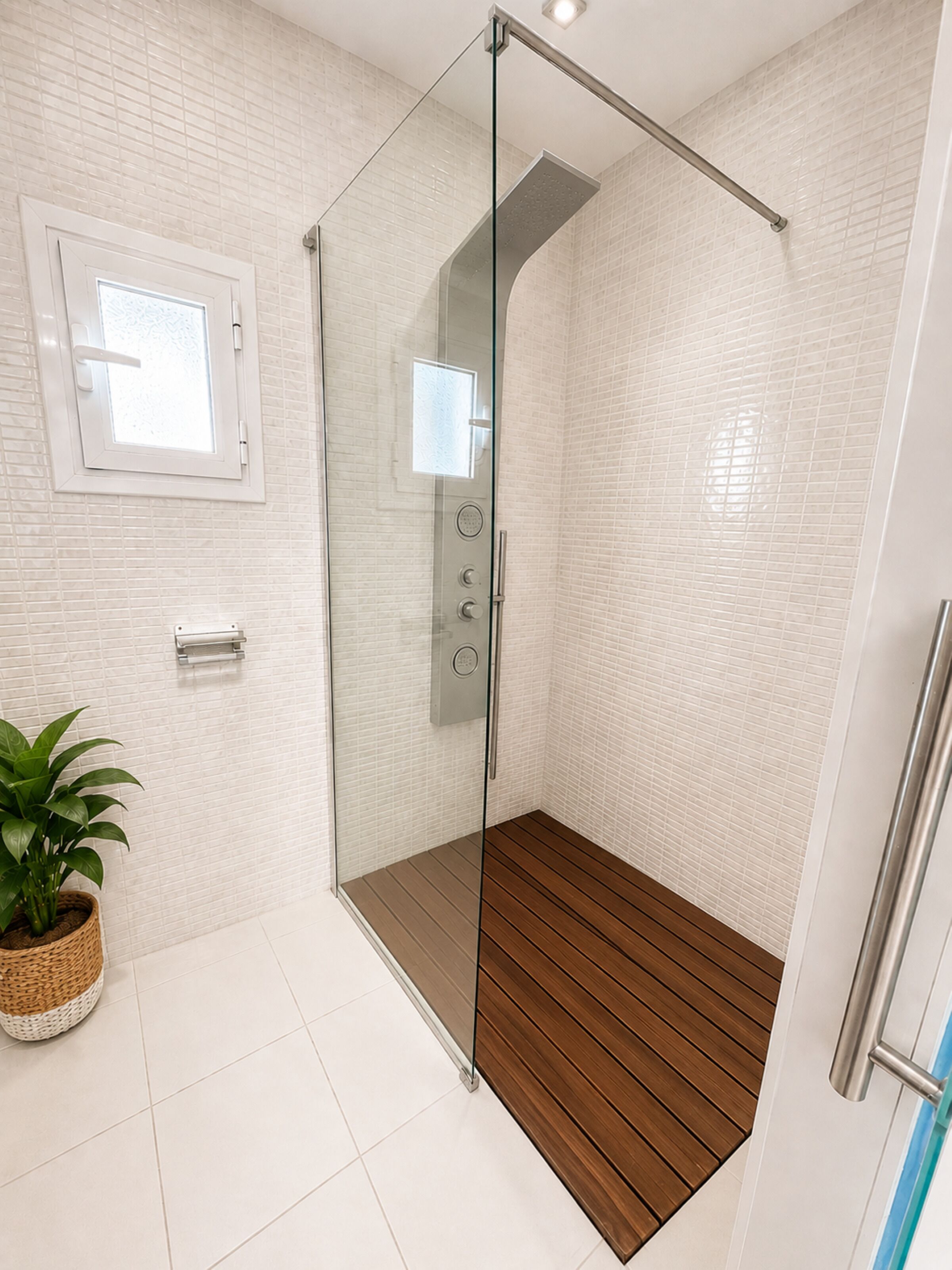 Een moderne badkamer met een glazen douchecabine, witte betegelde muren, een houten vloer en een kamerplant.
