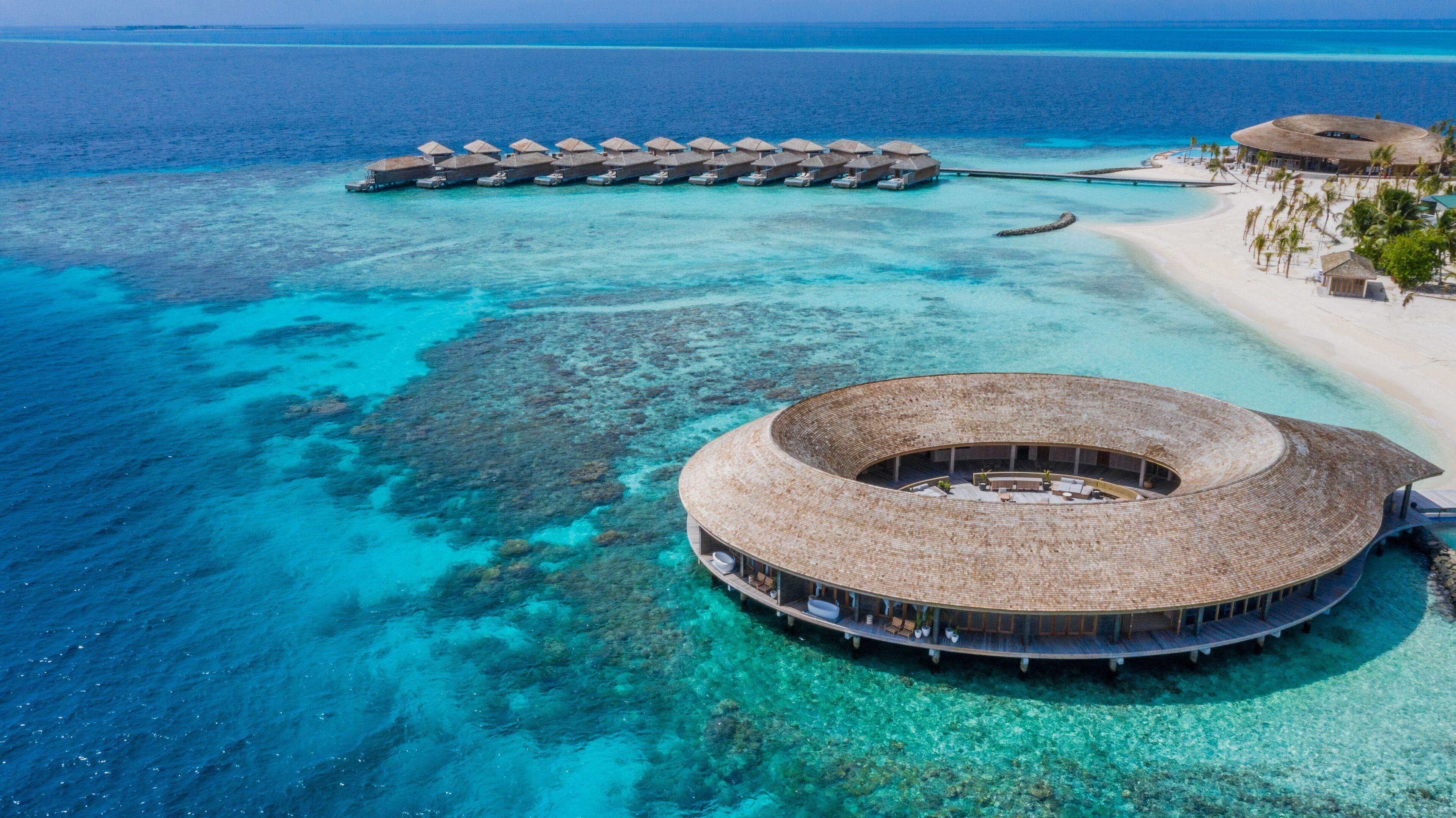 An overwater bungalow with a circular structure, connected to the beach by a pier.