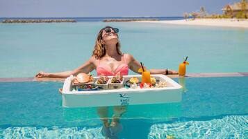 A person relaxing in a pool with a tray of food and drinks.