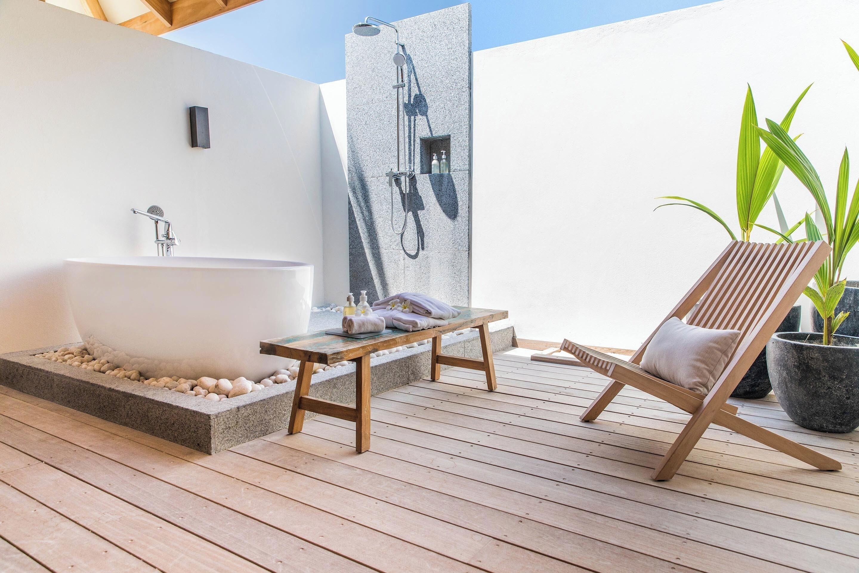 Una terraza de madera con una bañera, un banco y una silla de lounge.