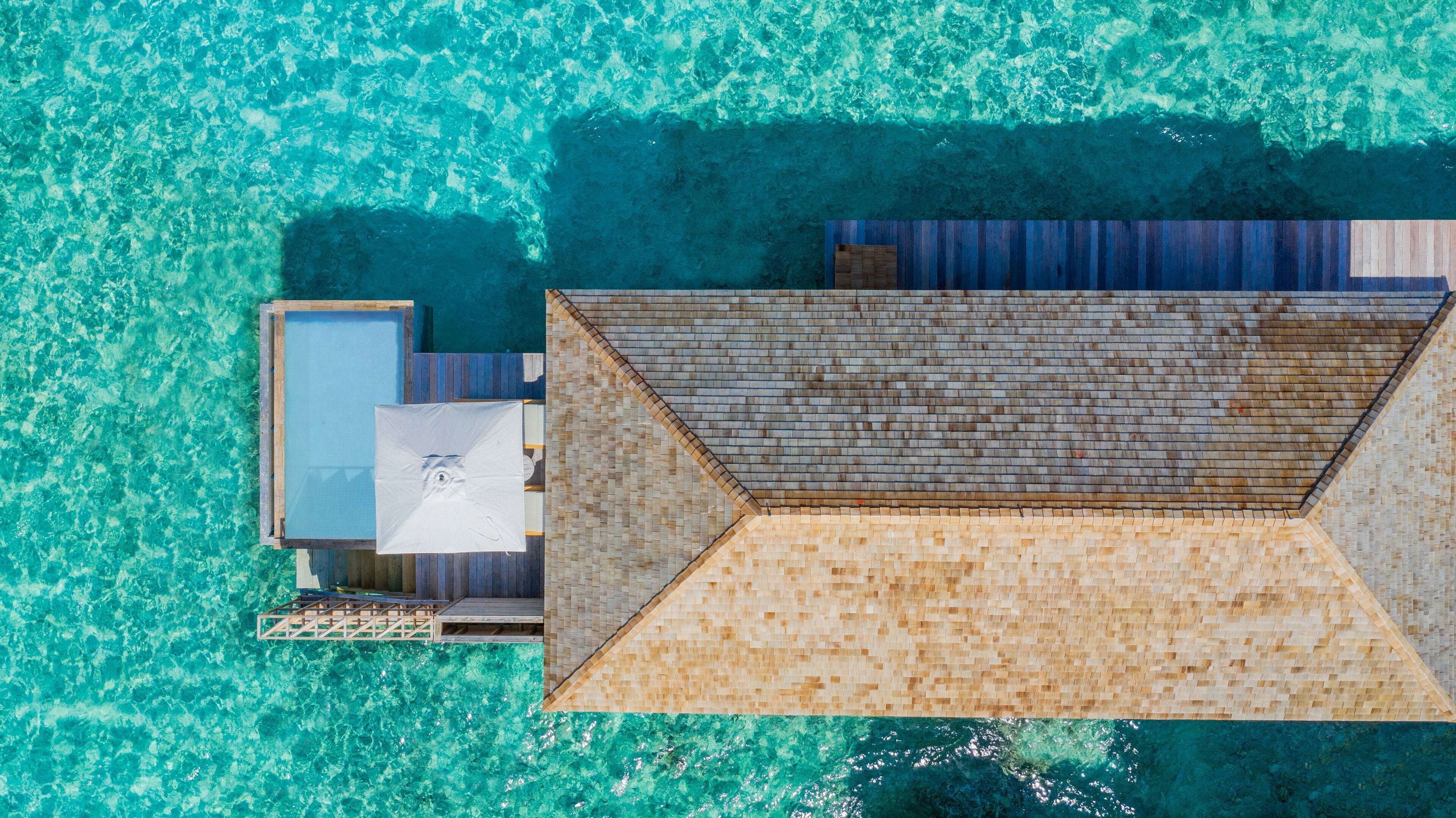 Vue aérienne d’un complexe hôtelier doté d’une piscine, d’une terrasse en bois et d’un espace salon abrité.