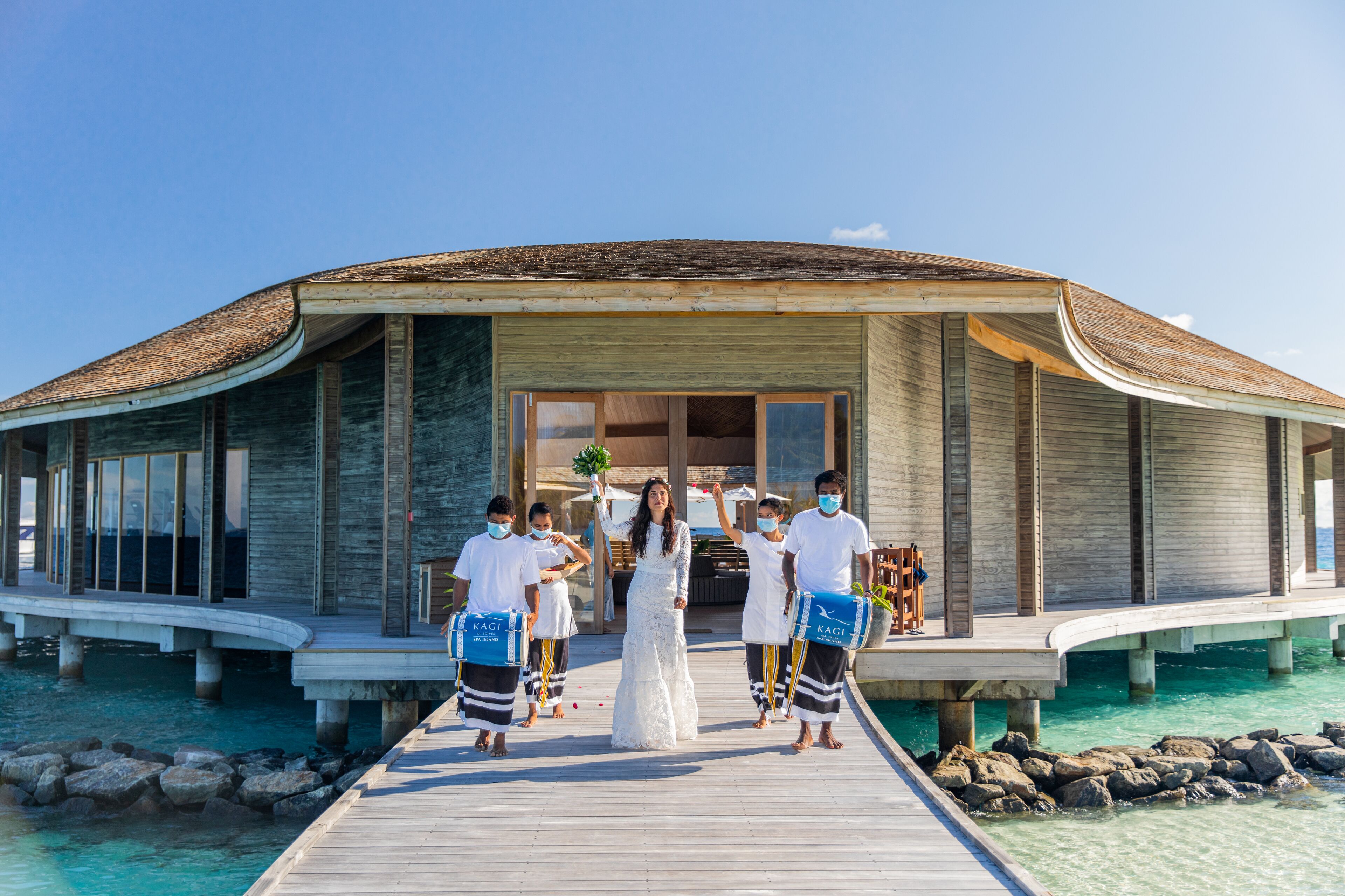 A wooden overwater villa with a curved roof, a wooden deck, and clear turquoise water.