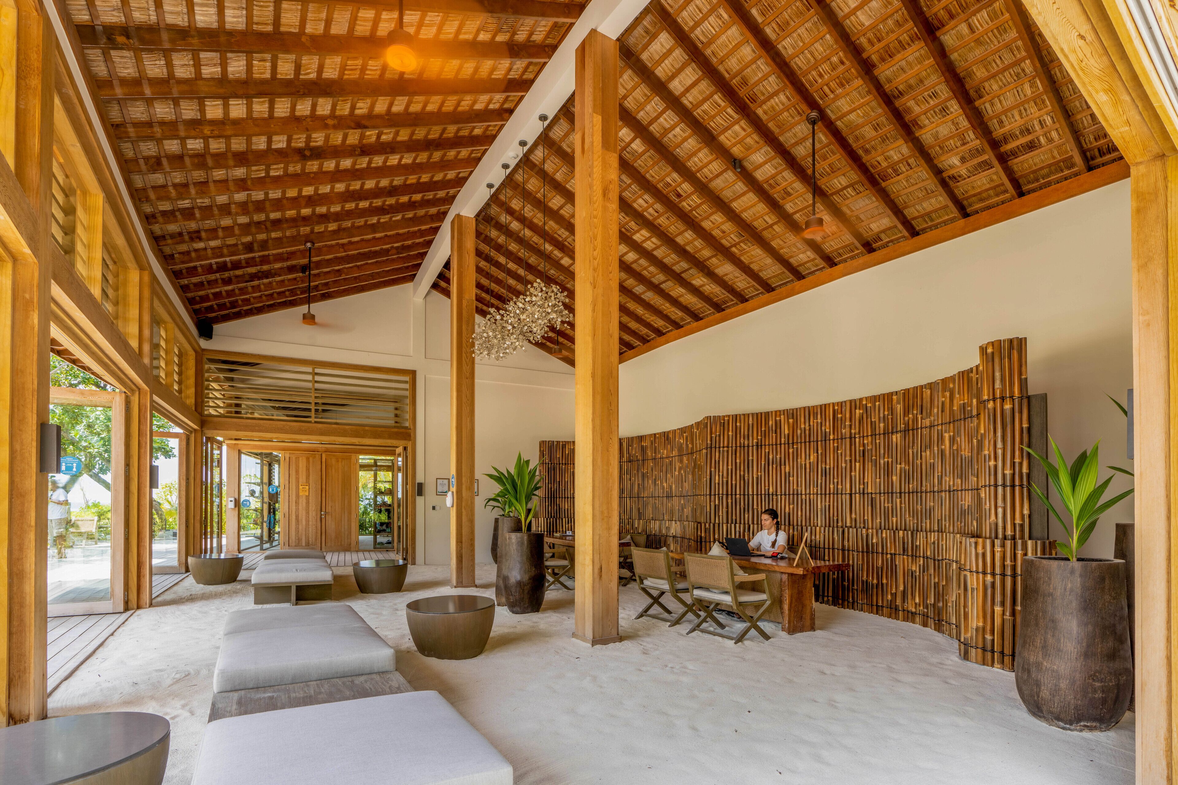 A spacious lobby with a high wooden ceiling, large seating areas, and a bamboo wall.