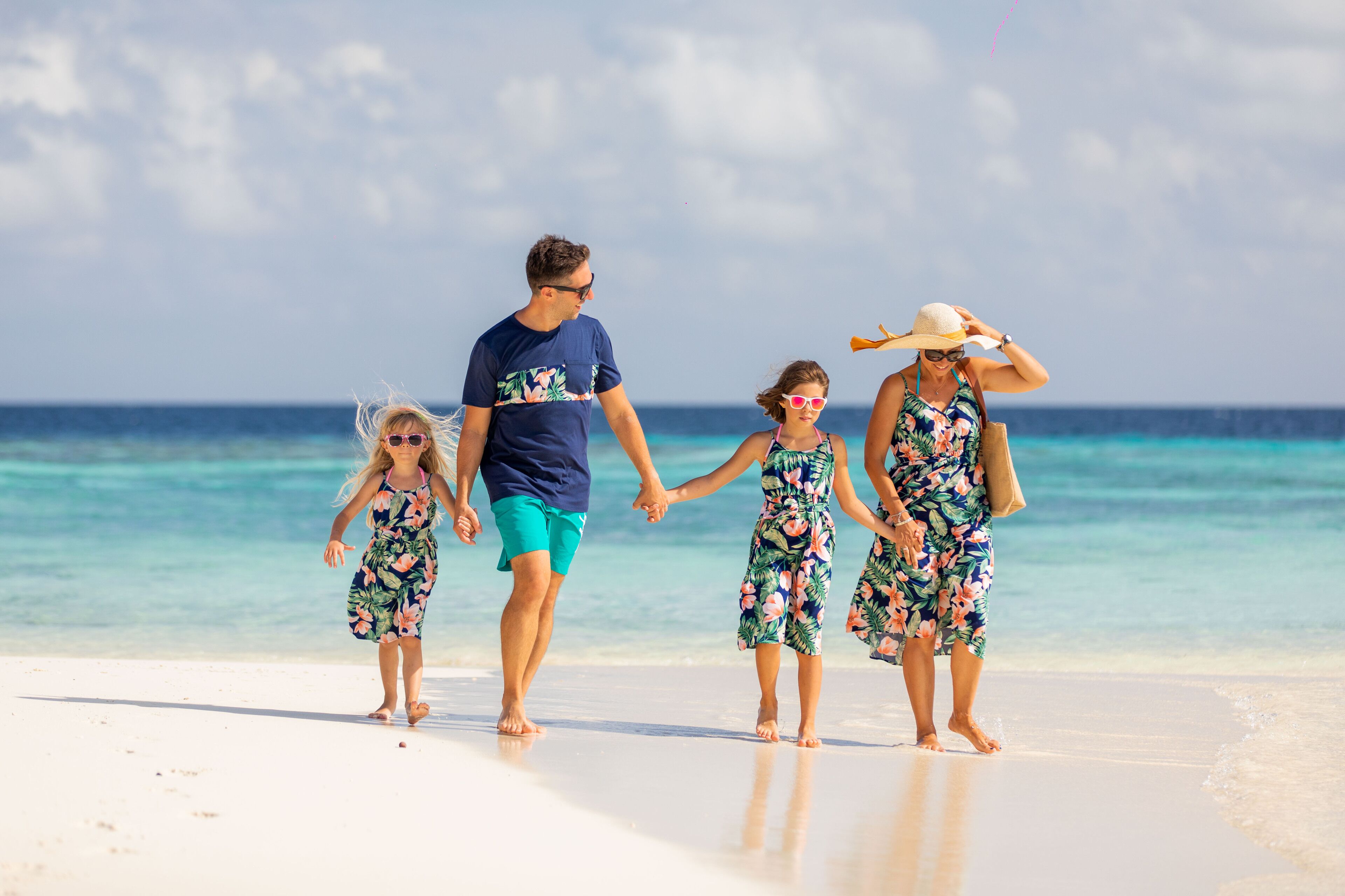 Una familia caminando por la playa bajo cielos despejados y aguas tranquilas.