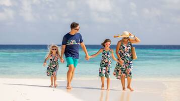 Una familia caminando por la playa bajo cielos despejados y aguas tranquilas.