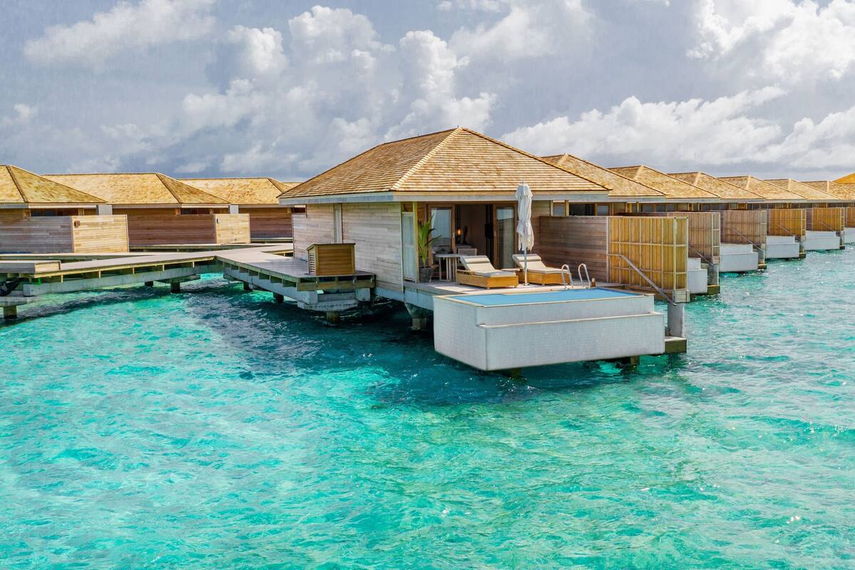 Overwater bungalows with a pool, wooden deck, and lounge chairs.
