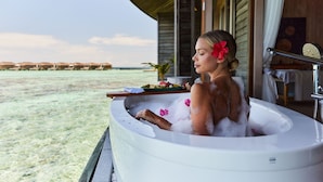 A person relaxing in a bathtub with a view of a beach and overwater bungalows. - Kagi Maldives Resort & Spa (Kagi Island)