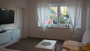 Et værelse med fjernsyn på et skab, gardiner foran et vindue, et lille bord og en seng.
