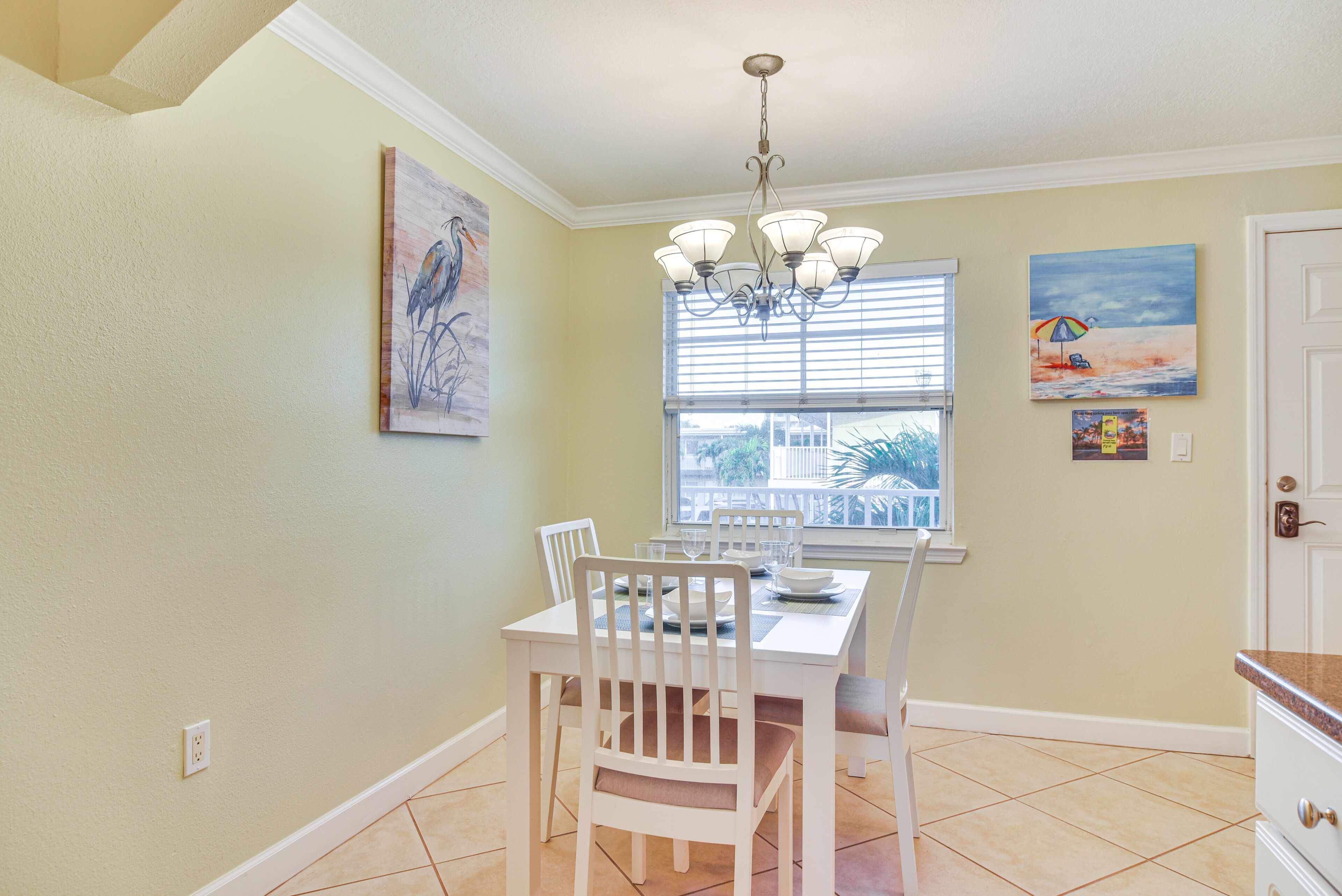 A dining area with a white table and chairs, a chandelier, and artwork on the walls.